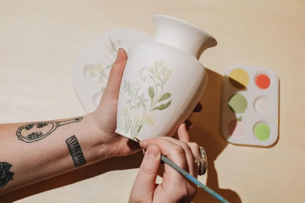 Artist painting delicate flowers on a ceramic vase