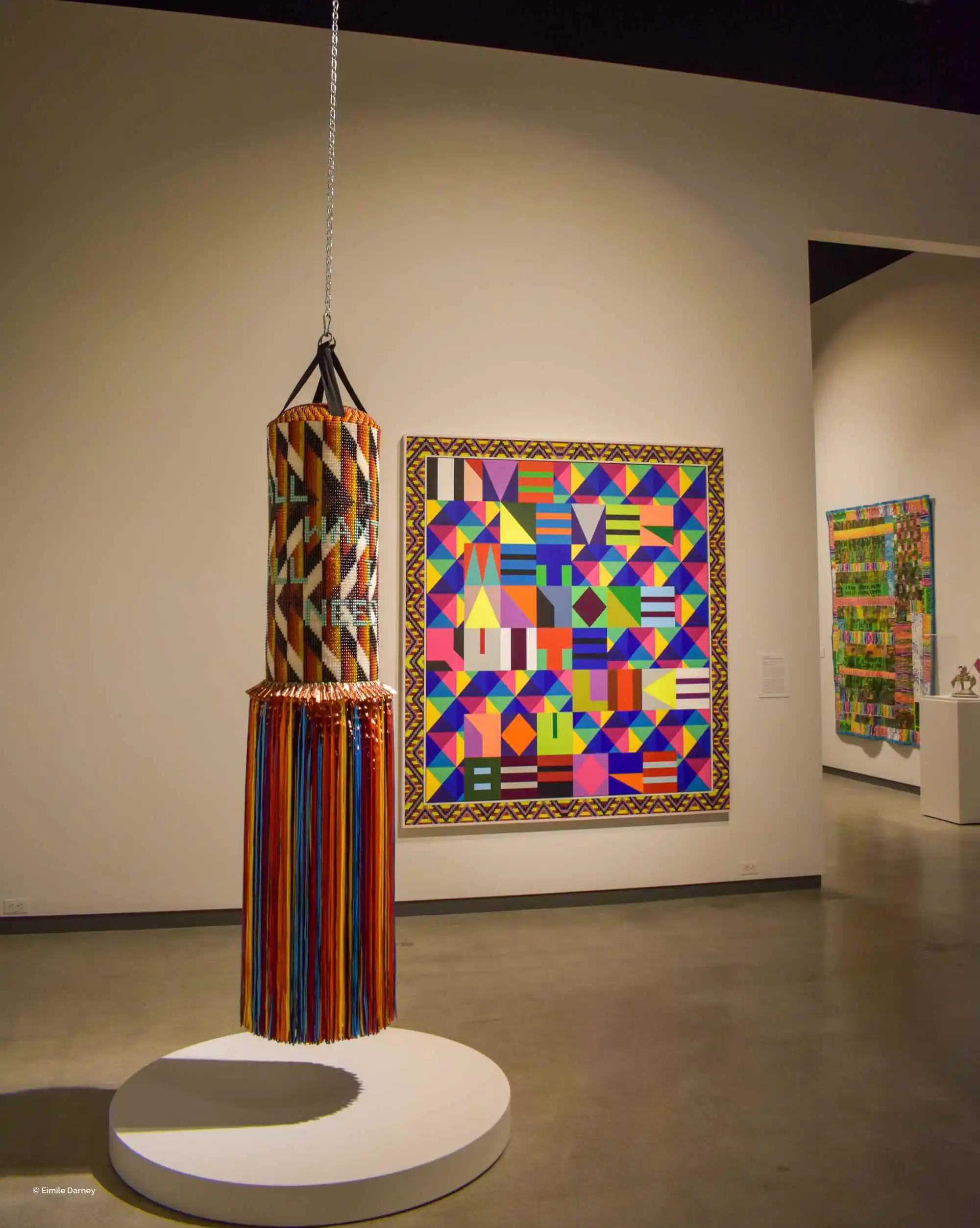 Colorful textile punching bag and geometric artwork displayed in a museum